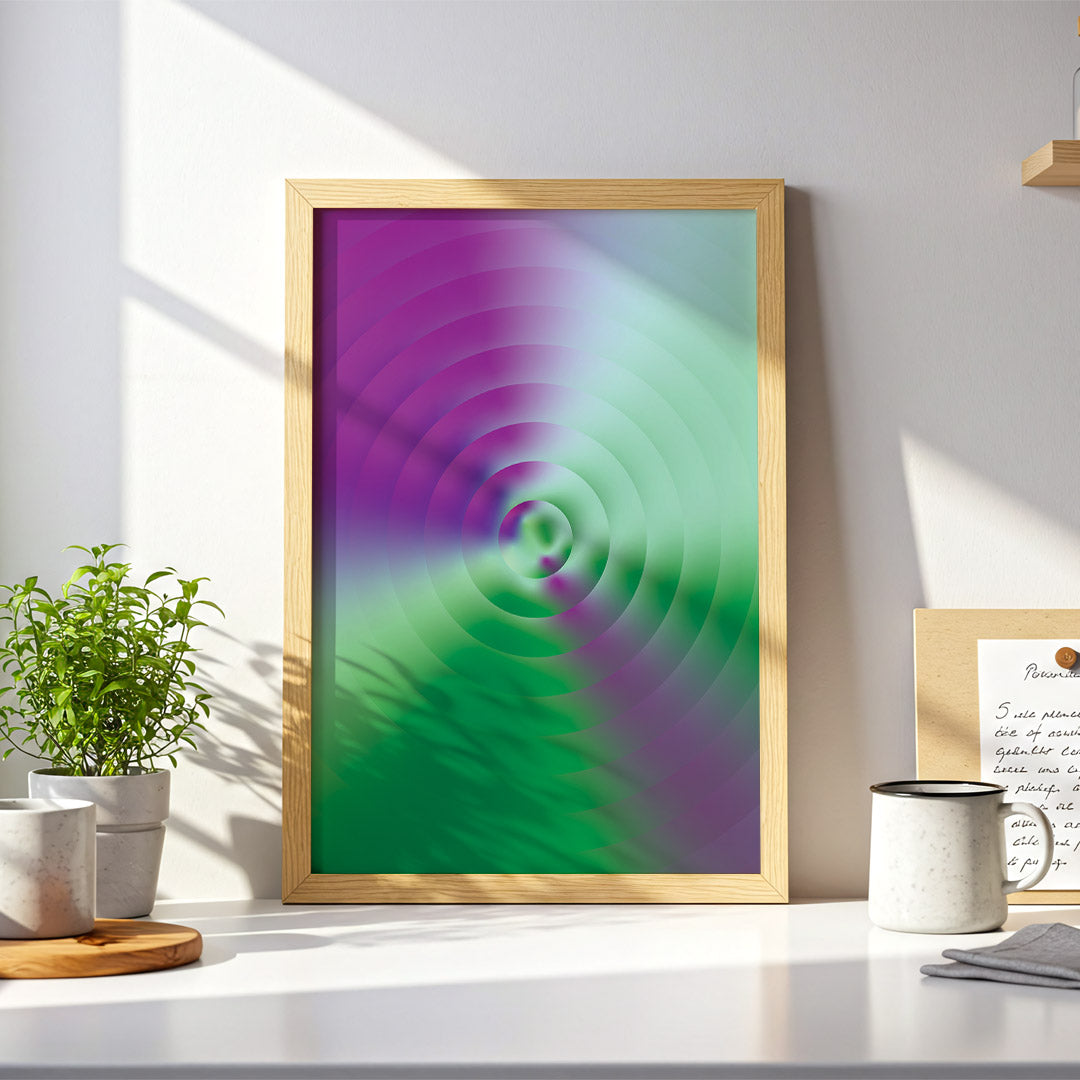 Framed abstract art with purple and green colors on a desk with plants and a mug.